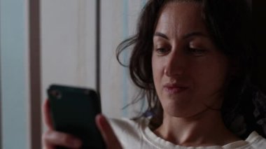 Kız yatağa oturur ve akıllı telefona bakar.