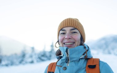 Dişlerinde diş telleri olan gülümseyen bir kadın, bir kızın portresi kış dağlarının ve karla kaplı ağaçların arkasında.