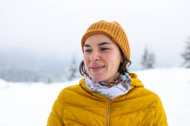 Dişlerinde diş telleri olan gülümseyen bir kadın, bir kızın portresi kış dağlarının ve karla kaplı ağaçların arkasında.