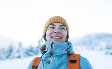 Dişlerinde diş telleri olan gülümseyen bir kadın, bir kızın portresi kış dağlarının ve karla kaplı ağaçların arkasında.