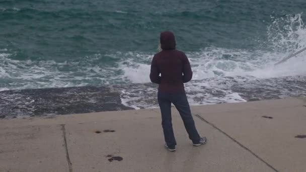 Una mujer se para en la orilla y mira al océano, las olas de tormenta rompen en la orilla — Vídeo de stock
