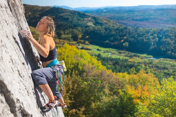 少女ロッククライマー秋の森と青空を背景に岩を登る 登山者は道具を使って難しい道を歩きます — ストック写真