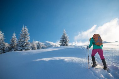 Kar ayakkabılı bir kadın karlı bir dağa tırmanıyor, kış yürüyüşü, yürüyüş ekipmanları.