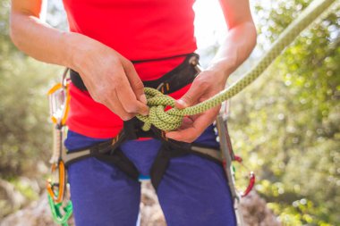 Kaya tırmanışçısı bir kız dağlarda güvenli bir tırmanış yapmak için kendini iple bağlıyor. Sporda güvenlik. Kaya tırmanışı için hazırlık. Sokaklarda spor yapıyor..