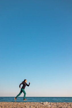 Sabah koşusu yapan bir kız, deniz kıyısında spor yapmak için koşan bir kadın, kumsalda koşan bir atlet.