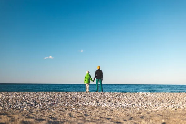 一个带着孩子的女人沿着海岸散步 一个带着儿子在海滩上的母亲 一个男孩和一个母亲看着海浪 — 图库照片