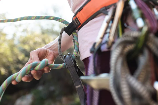 A rock climber prepares equipment for climbing, a woman holds a rope in her hands, a climber ties a knot