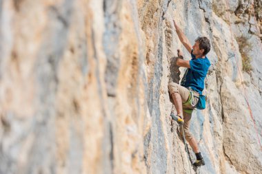 Güçlü bir adam yüksek irtifada bir kayaya tırmanır, kayalıklarda bir dağcı treni, eğitim gücü ve dayanıklılık.