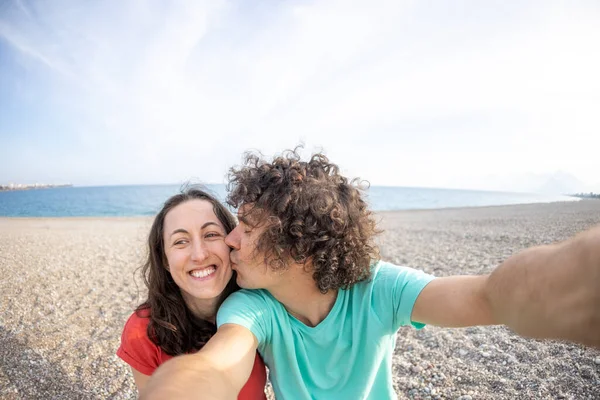 Bir adam ve bir kadın sahilde selfie çekiyor, bir aile denizde dinleniyor, aşıklar sahilde fotoğraf çekiyor.