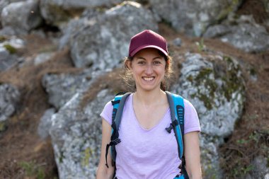 Gülümseyen mutlu kız sırtında bir çantayla ormanda yürüyor. Ormanda kamp yapmak.