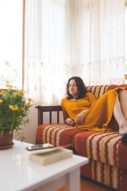 A girl in a yellow dress lies on the sofa, a woman is resting at home, home comfort