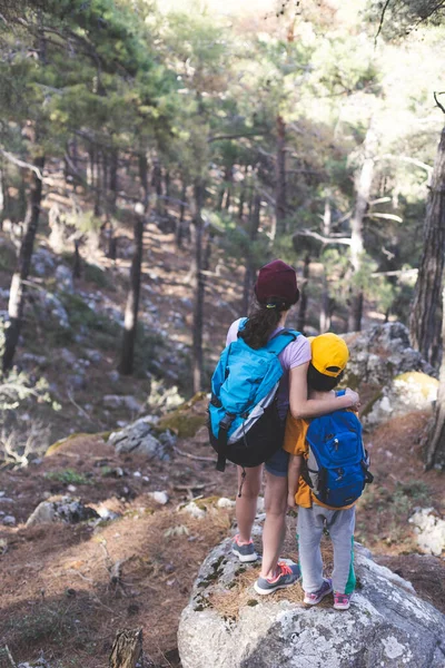 女性は彼女の息子と一緒に森を歩きます 彼の母親と少年はハイキングに行きます バックパック付きの子供は公園にあります 子供と一緒に旅行 子供は母親の手を持っています マウンテントレイル 母の日 — ストック写真