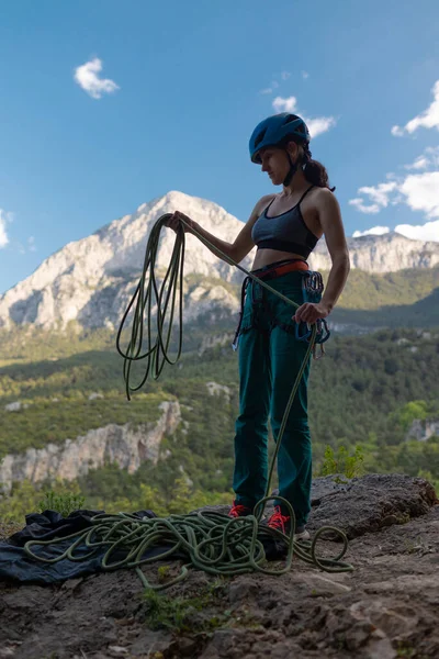 ヘルメットの女性は大きな山の背景にロープをコイル ロッククライマーはロッククライミングのための機器 安全装置を準備します — ストック写真