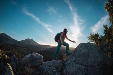 Sırt çantalı bir kadın dağa tırmanır, dağlarda yürüyüş yapar, hedefe ulaşmada başarı elde eder, gün batımında bir dağın arka planına karşı bir kızın silueti