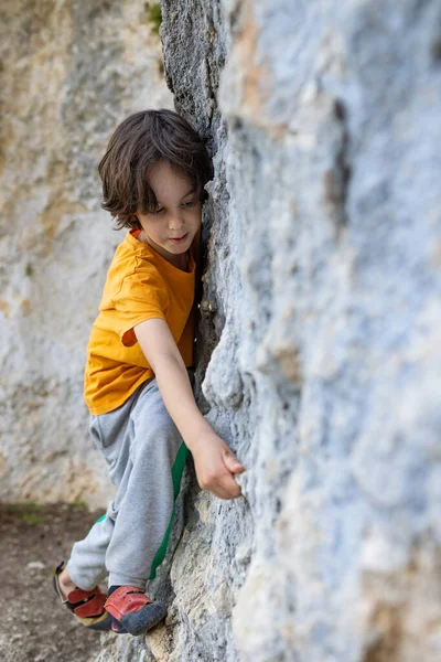 一个男孩爬岩石 一个小攀岩者正在训练爬大石头 一个孩子去参加体育活动 — 图库照片
