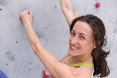 Gülümseyen kız tırmanma duvarına tırmanıyor, kadın ekstrem sporlarla meşgul, şehirde kaya tırmanışı, güç ve dayanıklılık eğitimi alıyor.