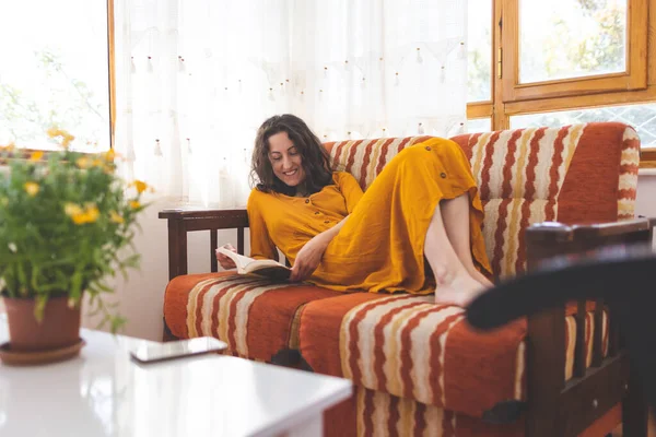 The girl lies on the sofa and reads a book, a young woman in a dress reads at home