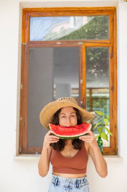 Hasır şapkalı gülen kız karpuz yiyor, elinde karpuz dilimi tutan kadın