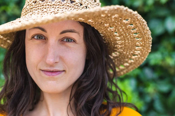 Hasır şapkalı gülümseyen bir kız sarmaşıkla kaplanmış bir duvarın yanında duruyor. Siyah saçlı bir kadının portresi.