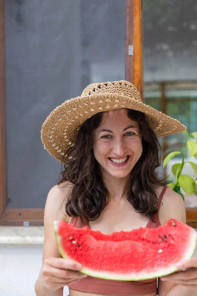 Hasır şapkalı gülen kız karpuz yiyor, elinde karpuz dilimi tutan kadın