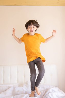 Enerjik bir çocuk yatakta zıplıyor, pijamalı bir çocuk odasında oynaşıyor, çocuk hafta sonunun tadını çıkarıyor.