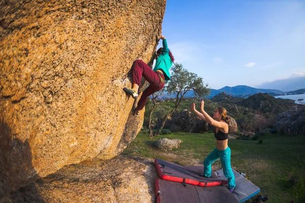 Friends go in for sports in nature, bouldering on rocks, girl climbs a big stone, woman is belayng partner, outdoor recreation, bouldering on the
