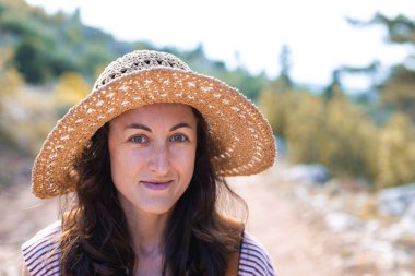 Ormanda sırt çantası ve hasır şapkalı bir kadının portresi, yürüyüş yapan gülümseyen bir kız, yaz yürüyüşü yapan, ormanda gezmekten zevk alan mutlu bir kadın.