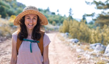 Ormanda sırt çantası ve hasır şapkalı bir kadının portresi, yürüyüş yapan gülümseyen bir kız, yaz yürüyüşü yapan, ormanda gezmekten zevk alan mutlu bir kadın.