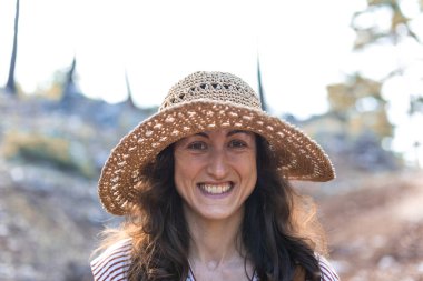 Ormanda sırt çantası ve hasır şapkalı bir kadının portresi, yürüyüş yapan gülümseyen bir kız, yaz yürüyüşü yapan, ormanda gezmekten zevk alan mutlu bir kadın.