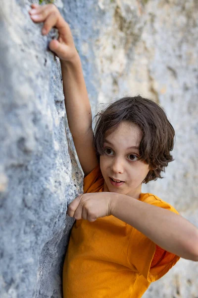 A boy climbs a rock, a little rock climber is training to climb a boulder, a child goes in for sports