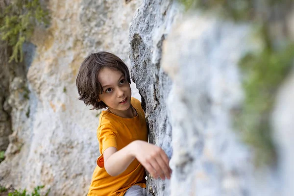 A boy climbs a rock, a little rock climber is training to climb a boulder, a child goes in for sports