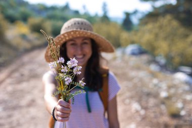 Hasır şapkalı bir kız elinde bir buket yaban çiçeği tutuyor, gülümseyen bir kadın elinde buket tutuyor, doğada bir yürüyüş.