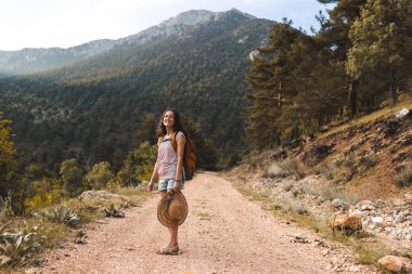 Dağ yolunda sırt çantalı bir kadın, dağlarda bir yürüyüş, orman yolunda yürüyen şapkalı bir kız, gülümseyen bir esmer