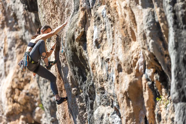 A woman climbs a rock, a strong girl trains strength and endurance, extreme sport, rock climbing on natural terrain, a rock climber climbs with a rope