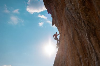 Kaya tırmanışçısı kaya tırmanışı, olimpiyat sporu yapan adam doğal arazi, güç ve dayanıklılık eğitimi, yüksek dağların arka planında kaya tırmanıcısı ve mavi gökyüzü.