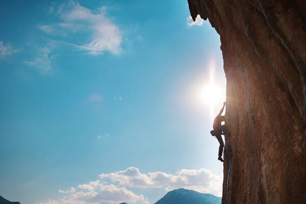 Rock climber climbing rock, man doing olympic sport on natural terrain, strength and endurance training, rock climber on the background of high mountains and blue sky
