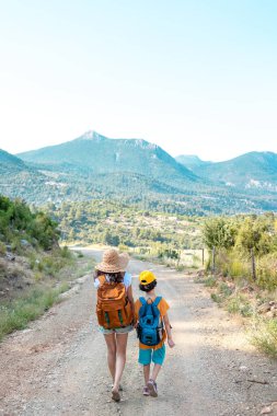Sırt çantalı bir kadın, bir çocuğu dağ yolunda elinden tutar ve bir çocuk annesiyle seyahat eder. Çocuklarla yürüyüş, resimli yerlere seyahat.