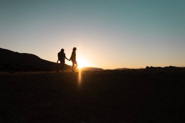 Gün batımında dağlarda seyahat ederken sırt çantalı iki kızın silueti. Gün batımında iki kişi dağ sıraları boyunca yürür. Özgürce seyahat et..