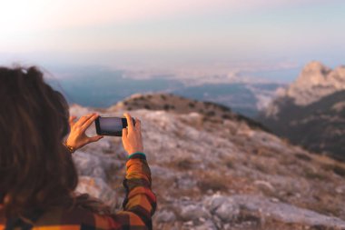 Güzel genç kız seyahat eder ve telefonda fotoğraf çeker. Dağlarda dolaşmak. Gün batımında elinde telefon olan bir kızın portresi..