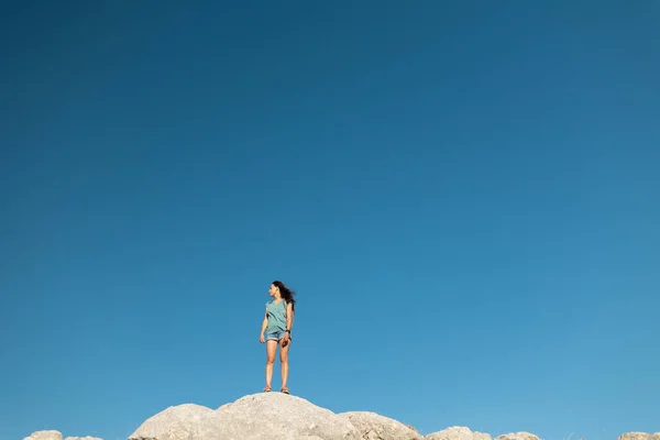 the girl stands against the background of the blue sky. joyful young girl stands on top of the mountain. a trip to the mountains.