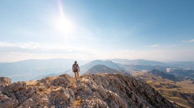 A girl walks along a mountain road against the blue sky and mountains. travel and adventure in the mountains. Alpinism and rock climbing