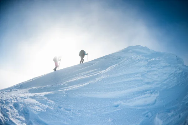 climbing a snow-covered mountain during a snow storm, two women in winter trekking, climbers climb to the top of the mountain in winter