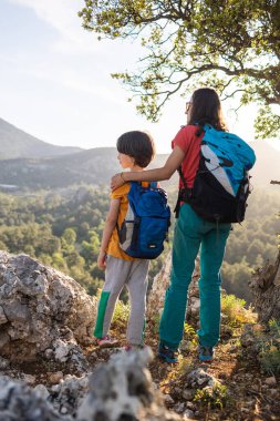 Oğlan ve annesi dağın tepesinde duruyorlar, bir kadın çocukla seyahat ediyor, çocuk annesiyle dağlara bakıyor, sırt çantalarıyla seyahat ediyor, yürüyüş yapıyor ve çocuklarla tırmanıyor.