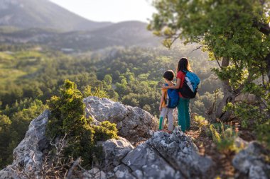 Oğlan ve annesi dağın tepesinde duruyorlar, bir kadın çocukla seyahat ediyor, çocuk annesiyle dağlara bakıyor, sırt çantalarıyla seyahat ediyor, yürüyüş yapıyor ve çocuklarla tırmanıyor.