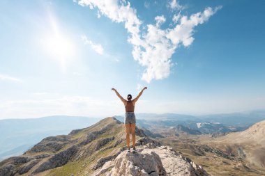 Kız mavi gökyüzünün arka planında duruyor. Neşeli genç kız dağın tepesinde duruyor. Dağlara bir gezi..