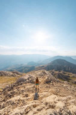 A girl walks along a mountain road against the blue sky and mountains. travel and adventure in the mountains. Alpinism and rock climbing