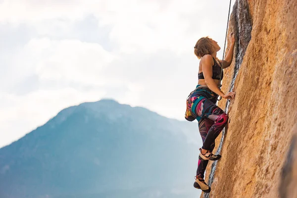 A woman climbs a rock, a strong girl trains strength and endurance, extreme sport, rock climbing on natural terrain, a rock climber climbs with a rope