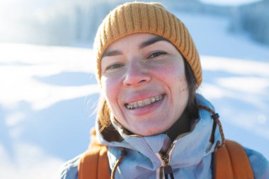 Dişlerinde diş telleri olan gülümseyen bir kadın, bir kızın portresi kış dağlarının ve karla kaplı ağaçların arkasında.
