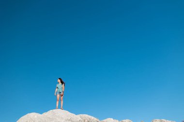 Kız mavi gökyüzünün arka planında duruyor. Neşeli genç kız dağın tepesinde duruyor. Dağlara bir gezi..