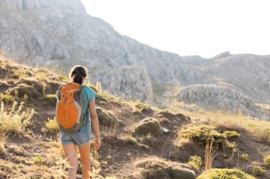a young girl with a backpack walks along a mountain path. travel and freedom